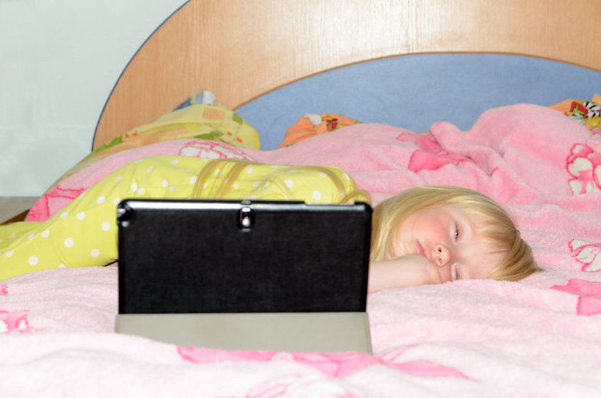 41217884 - cute blond little girl lying on her stomach while sleeping on her bed with tablet computer on a stand