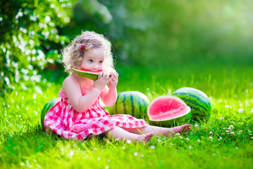 40333368 - child eating watermelon in the garden. kids eat fruit outdoors. healthy snack for children. little girl playing in the garden holding a slice of water melon. kid gardening.