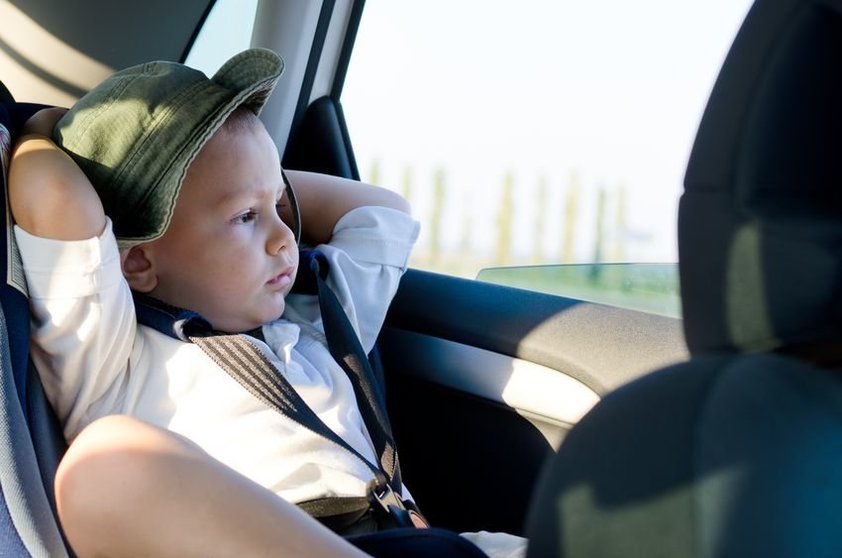 17657752 - little boy in a child safety seat sitting patiently in the back of a car with his hands behind his head staring out of the window