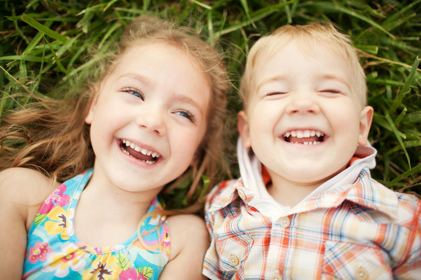 48126904 - top view portrait of two happy smiling kids lying on green grass. cheerful brother and sister laughing together.