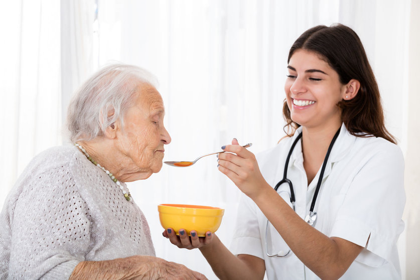 64951319 - happy female doctor feeding soup with spoon to senior patient in hospital