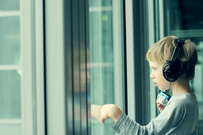 32226266 - boy with headphones looking out the window at the airport